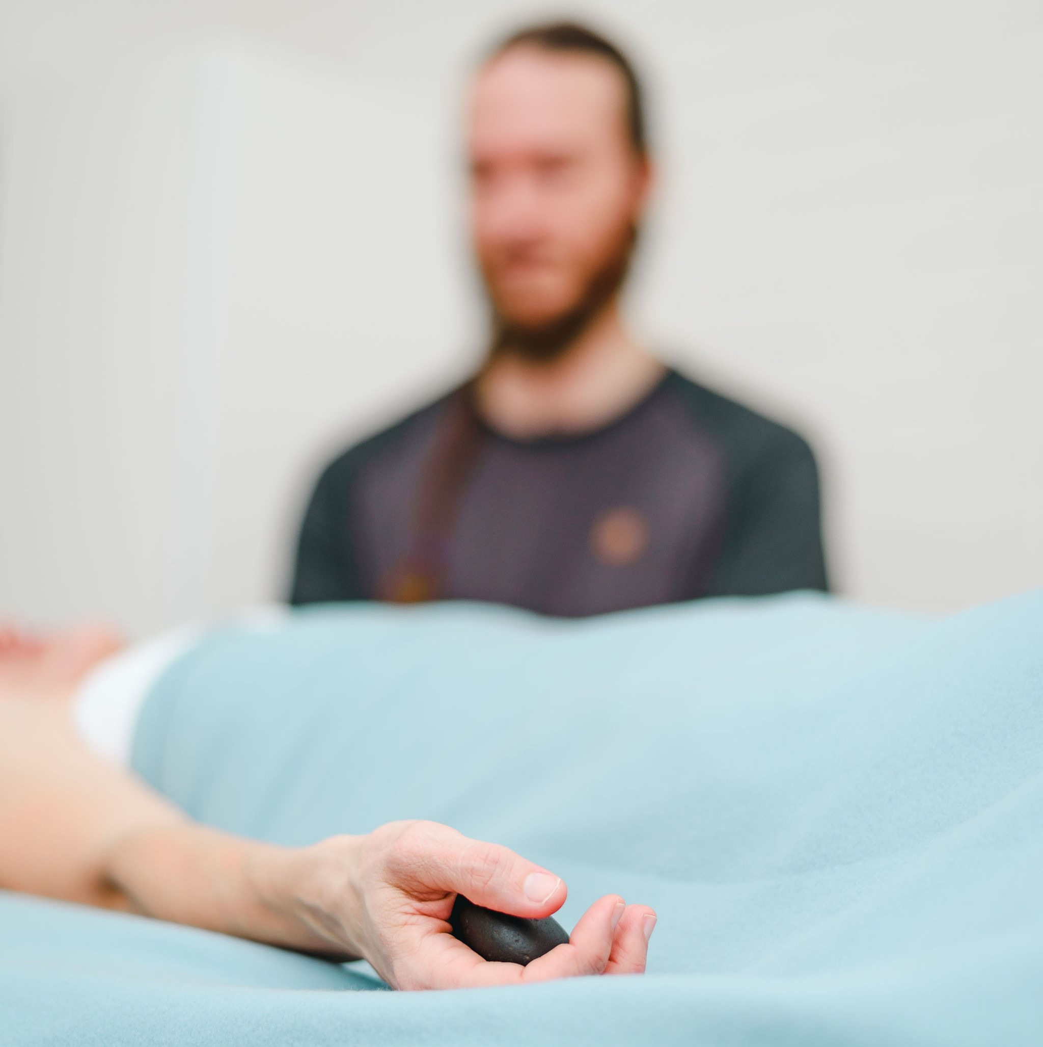 Massage therapist in the background, patient holding hot stone in hand foreground